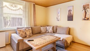 Un salon avec un canapé, une table sur laquelle est posée une nappe en dentelle, un radiateur et une fenêtre avec des rideaux.