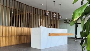 En receptionsdisk med en avskärmning av träribbor, ett vitt receptionsområde och hängande lampor.
