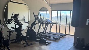 Ett gym med träningsutrustning, stora speglar och utsikt över bergen.