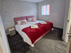 Een slaapkamer met een bed, kussens, een nachtkastje, een raam en een radiator.