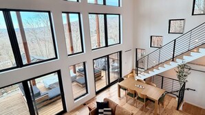 Amplia sala de estar con un ventanal grande, piso de madera, un sofá, una mesa de centro y una escalera.