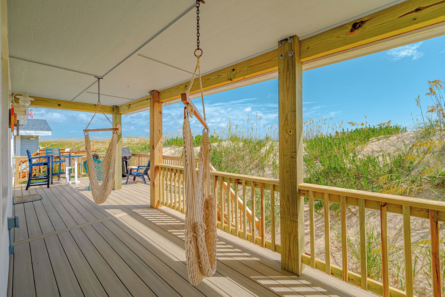 A wooden deck with a view of the beach, a hammock, and outdoor furniture.