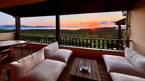 Un balcon avec un canapé, une table et une vue sur le coucher de soleil se déclinant sur un paysage.