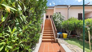 Un escalier menant à un bâtiment dont le sol est recouvert de carreaux, entouré de verdure et délimité par une clôture.