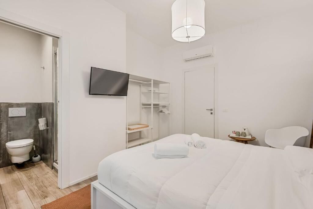 A hotel room with a bed, a TV mounted on the wall, a shower area, and a small table with a chair.