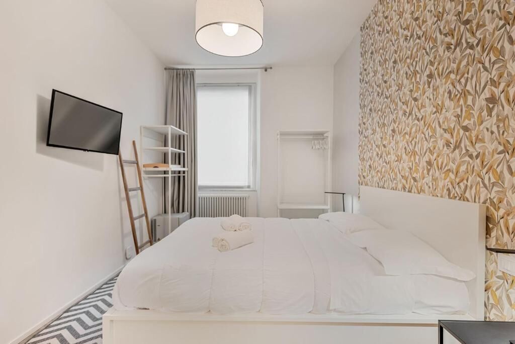 A hotel room with a bed, a TV mounted on the wall, a wardrobe, and a radiator.
