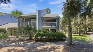 A two-story building with a balcony, surrounded by palm trees and a gravel driveway. - Pet-Friendly Shipyard Retreat | Pool & Tennis (Hilton Head Island)