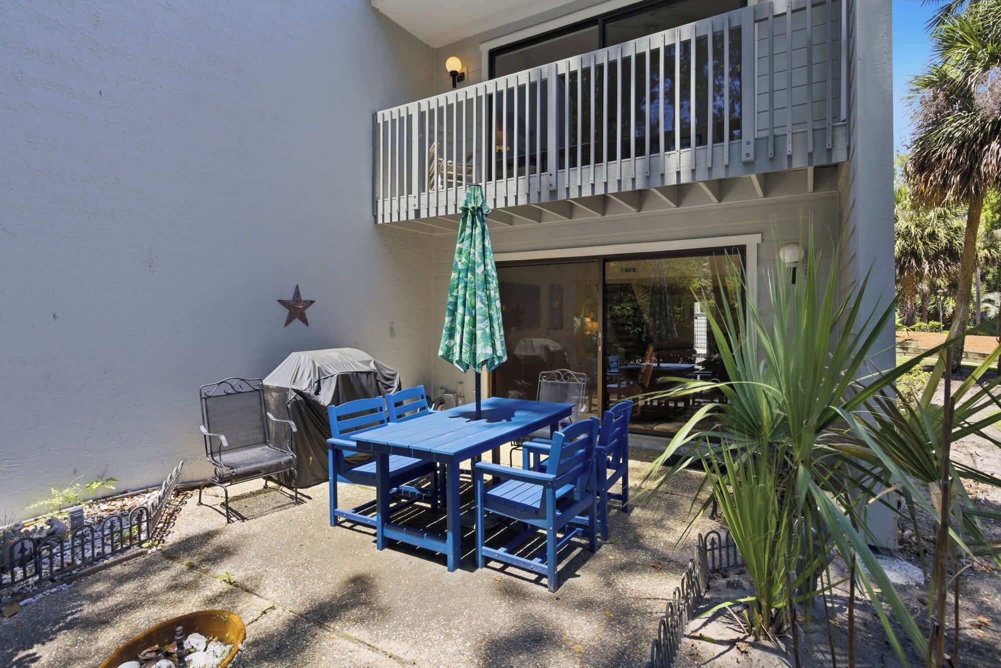 An outdoor patio with a blue table and chairs, a covered grill, and a star decoration on the wall.