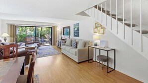 A spacious living area with a sofa, coffee table, and dining table, a staircase, and a view of greenery outside. - Pet-Friendly Shipyard Retreat | Pool & Tennis (Hilton Head Island)