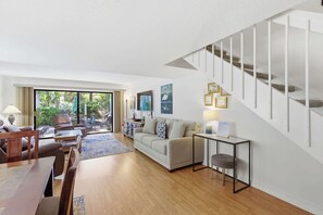 Amplia sala de estar con sofá, mesa de centro y mesa de comedor, una escalera y vistas al exterior.