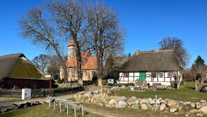 A traditional building with a thatched roof, stone walls, and a prominent tower. - Haus Boddenkieker 1 Rügen in Mönchgut – Ferienwohnung mit Meerblick und Südterrasse (Mönchgut)