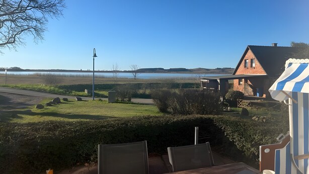 A house with a view of a lake, a street lamp, and a striped awning. - Haus Boddenkieker 1 Rügen in Mönchgut – Ferienwohnung mit Meerblick und Südterrasse (Mönchgut)