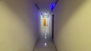 Un couloir d’hôtel avec une porte au bout, un interrupteur et une grille d’aération sur le mur.