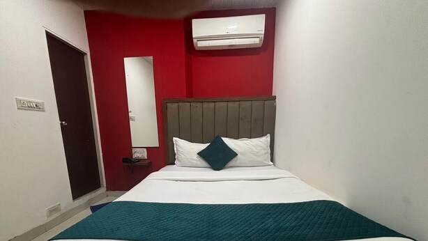 Une chambre d’hôtel avec un lit, un mur rouge, un plafond blanc et une fenêtre.