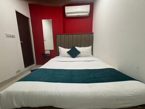 Una camera d'albergo con un letto, una parete rossa, un soffitto bianco e una finestra.