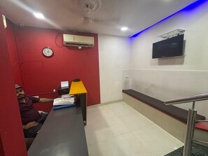 A room with a desk, a clock, an air conditioning unit, a television, and a red wall. - Hotel Zampex Executive (Mumbai)
