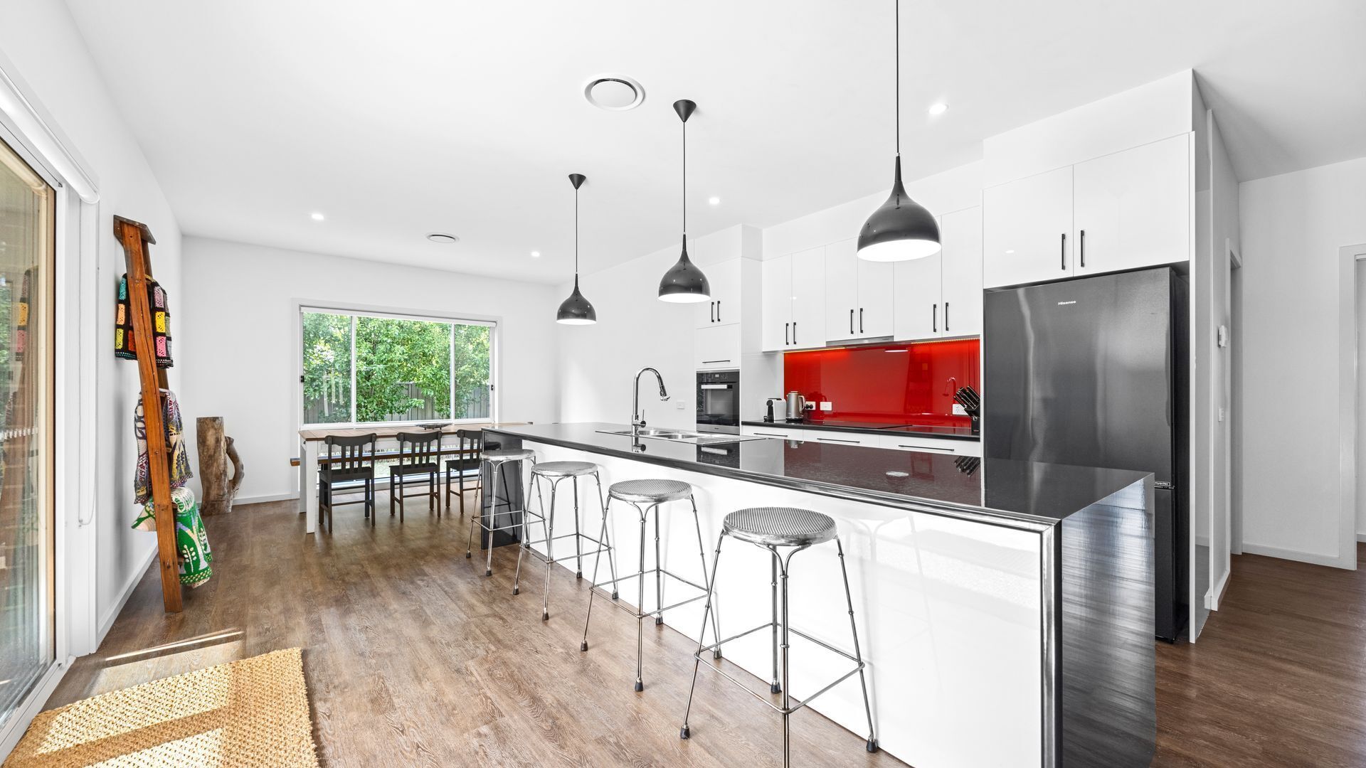 Une cuisine moderne dotée d’un îlot central, de tabourets de bar, de luminaires suspendus et d’un réfrigérateur en acier inoxydable.