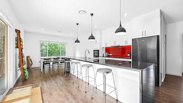 Une cuisine moderne dotée d’un îlot central, de tabourets de bar, de luminaires suspendus et d’un réfrigérateur en acier inoxydable.