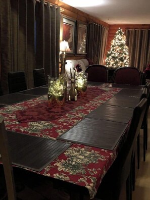 Een eetgedeelte met een lange tafel, stoelen, een kerstboom en een lamp.