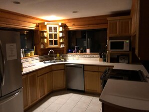 Een keuken met houten kastjes, een roestvrijstalen koelkast, een vaatwasser, een magnetron en een spoelbak.