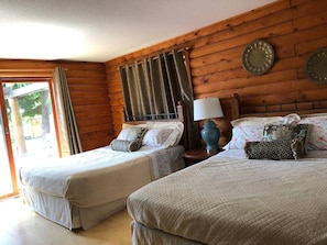 Habitació amb dos llits, paret de fusta, finestra amb cortines i una làmpada.