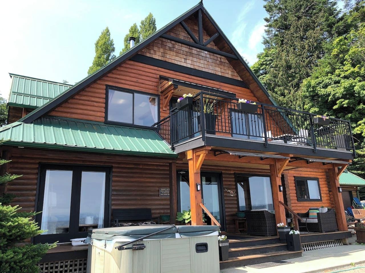 A two-story log cabin with a balcony, large windows, and a green roof.