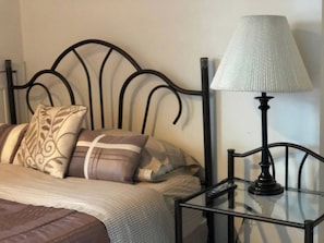 A bed with a headboard, pillows, a bedside table with a lamp, and a remote control.