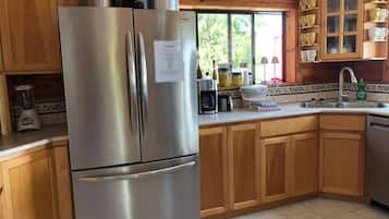 Une cuisine avec des meubles en bois, un réfrigérateur en acier inoxydable et une fenêtre donnant sur un paysage verdoyant.