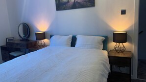 A bedroom with a bed, two bedside tables with lamps, a dresser, a mirror, and a painting on the wall. - Peaceful 1 bedroom house. Dog friendly, centrally located hidden gem. (Morpeth)