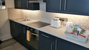 A modern kitchen with dark cabinets, a double sink, a built-in oven, and a countertop with a toaster and packaged snacks. - Peaceful 1 bedroom house. Dog friendly, centrally located hidden gem. (Morpeth)
