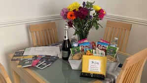 A dining table with a bottle, a vase with flowers, a parking pass, and some snacks. - Peaceful 1 bedroom house. Dog friendly, centrally located hidden gem. (Morpeth)