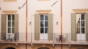 Fachada de edificio con varias ventanas, un balcón con sillas y una barandilla.