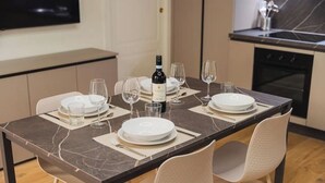 Una mesa de comedor servida con platos, vasos y una botella de vino, con sillas y una cocina al fondo.