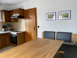 Een keuken met houten kastjes, een fornuis en een eethoek met een tafel en stoelen.