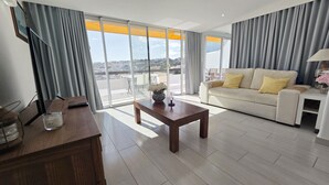 Una sala de estar moderna con sofá, mesa de centro, televisor y un balcón con vistas a la ciudad.
