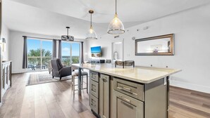 A modern kitchen with a large island, pendant lights, and a view of the outdoors. - 🏖️Large Balcony with Stunning Gulf Views | Pool | Calypso 2-301🏖️ (Panama City Beach)
