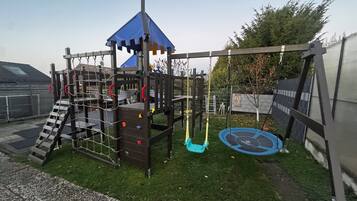 Ein Spielplatz mit Kletterwand, Schaukeln und Rutsche.
