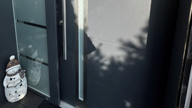 A modern building entrance with a glass door, a metal handle, and a small decorative snowman figure on the ground.