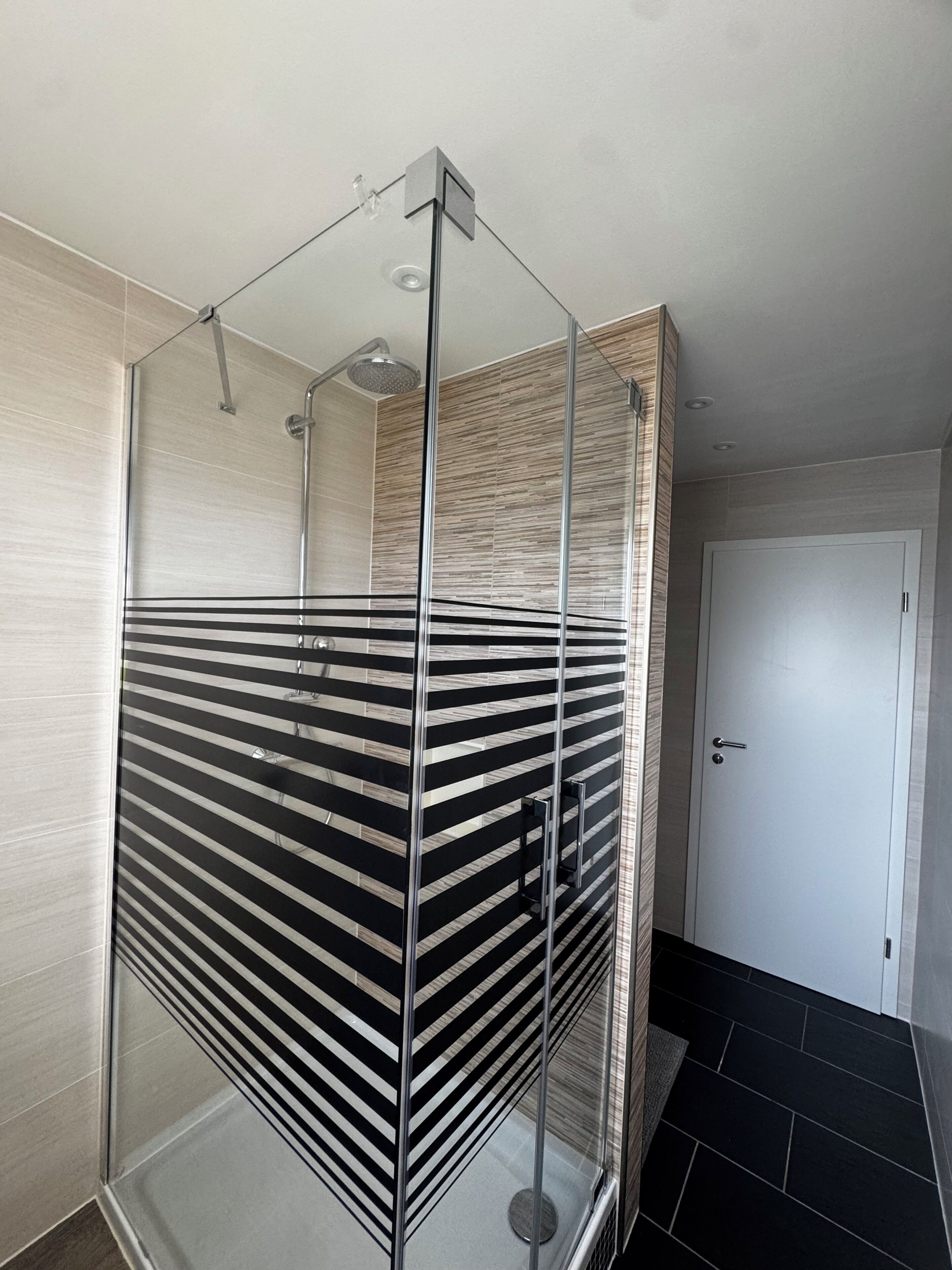 A modern bathroom with a glass shower enclosure, a white door, and a tiled floor.