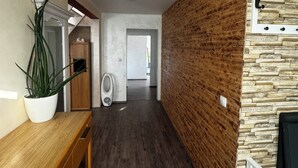 A hallway with a wooden bench, a potted plant, a white wall with a stone-like texture, and a white chair.