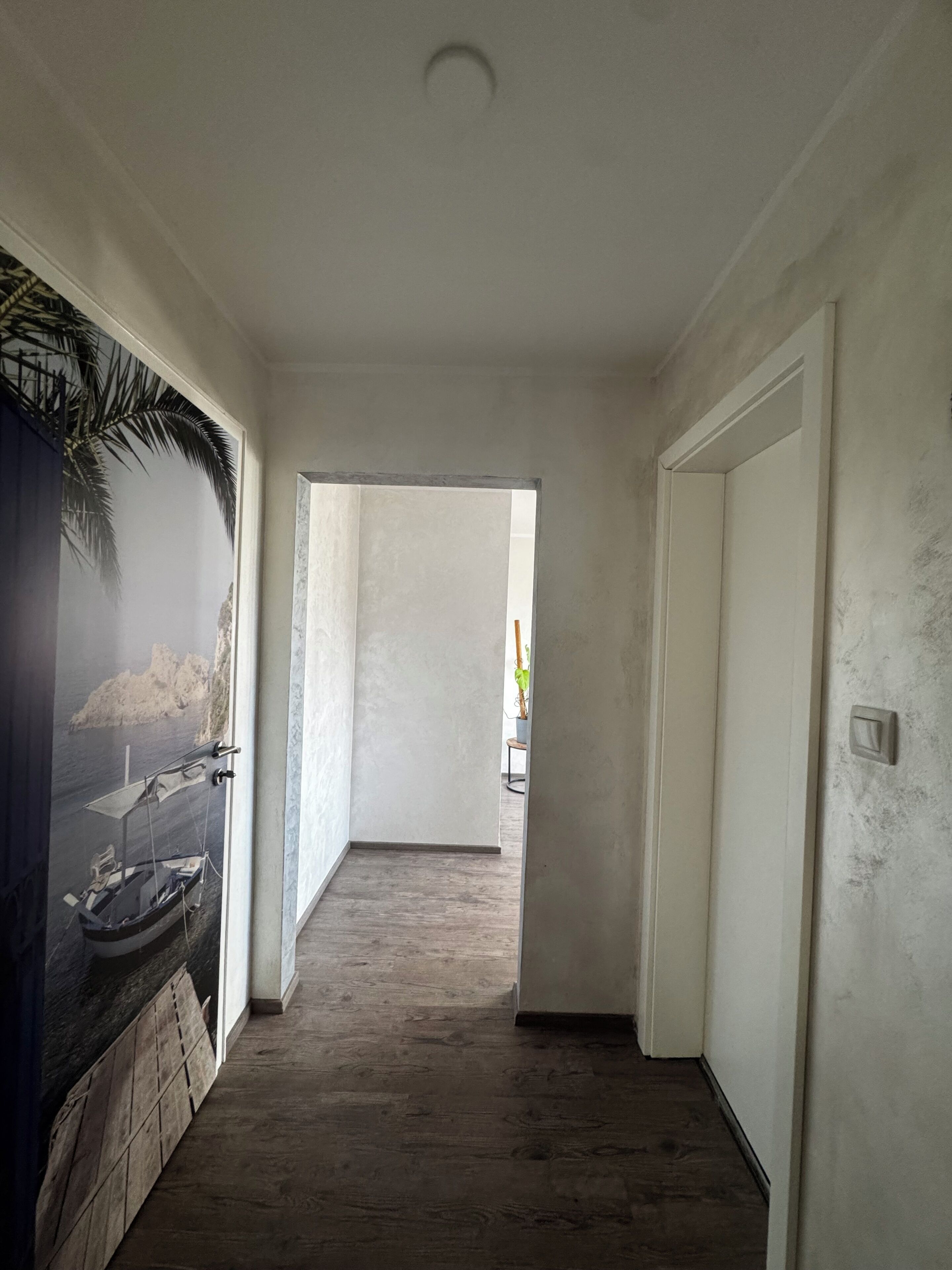 A hallway with a wooden floor, white walls, and a door on the right.
