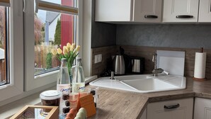 A modern kitchen with white cabinets, a large window, and a view of a garden.