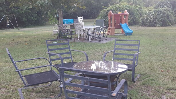 Un espace extérieur verdoyant avec une table en métal et quatre chaises, une balançoire et une structure de jeu avec un toboggan.