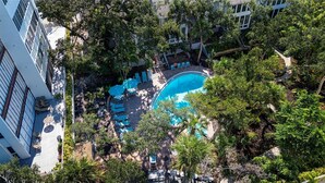 Luftaufnahme eines Hotels mit Schwimmbad, umgeben von üppigem Grün und Sitzgelegenheiten im Freien.