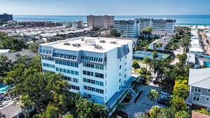Ein mehrstöckiges Hotel mit flachem Dach, umgeben von Grün und Blick aufs Meer.