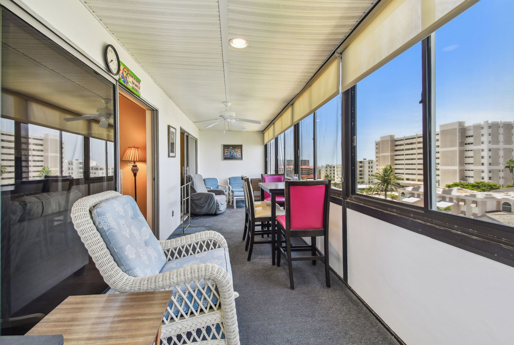 A balcony with wicker furniture, a table, and chairs. There is a view of buildings in the background.