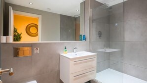 A modern bathroom with a glass shower enclosure, a white sink, and a toilet.