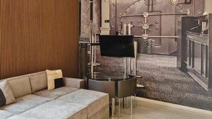 A modern living room with a sectional sofa, a flat-screen TV, and a wall mural of industrial machinery.