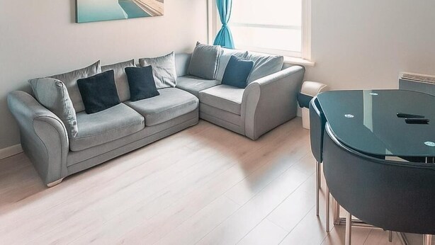 A modern living room with a sectional sofa, a glass dining table, and a large window with curtains.