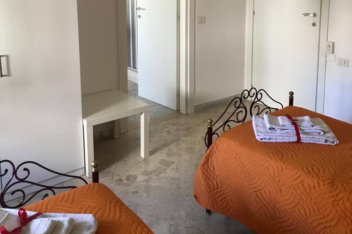 Habitación de hotel con dos camas, un banco, un armario y un equipo de aire acondicionado.